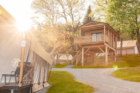 Alloggio glamping con tende di lusso e una casa in legno sopraelevata, circondata dalla natura.
