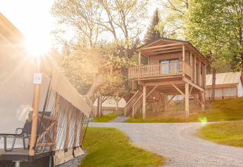 Alloggio glamping con tende di lusso e una casa in legno sopraelevata, circondata dalla natura.