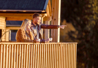 Een stel geniet van koffie op het terras van hun glampingaccommodatie en lacht naar het mooie uitzicht.