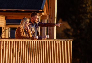 Una coppia si gode il caffè del mattino sulla terrazza del loro alloggio glamping, sorridendo al panorama.