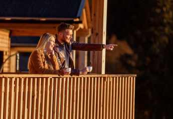 Een stel geniet van koffie op het terras van hun glampingaccommodatie en lacht naar het mooie uitzicht.