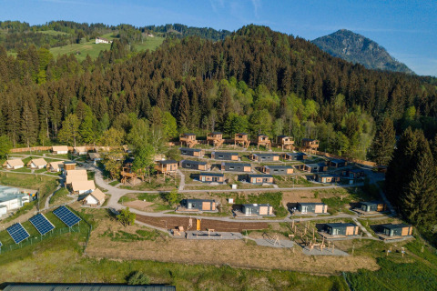 Vista aerea di un'area glamping con cabine e tende immerse nella natura tra boschi e montagne.