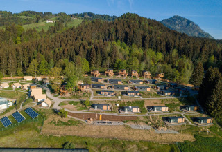 Vista aerea di un'area glamping con cabine e tende immerse nella natura tra boschi e montagne.
