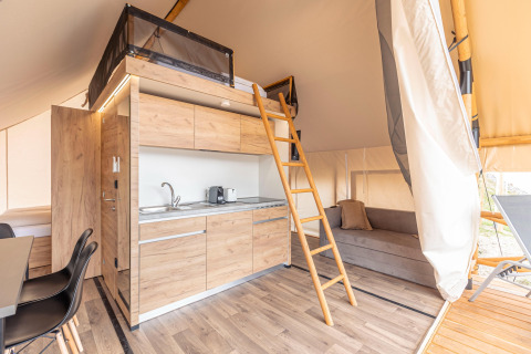 Interno della tenda safari Chalets & Glamping Nassfeld 6 in Austria con letto soppalcato, cucina e divano.