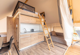 Interno della tenda safari Chalets & Glamping Nassfeld 6 in Austria con letto soppalcato, cucina e divano.