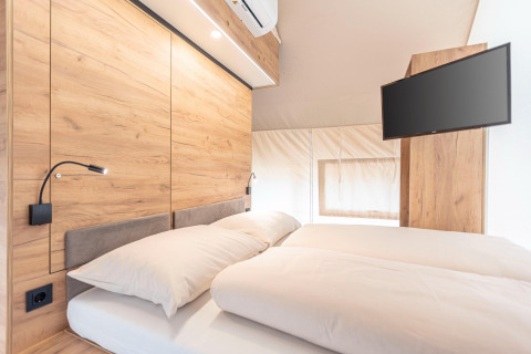 Camera moderna nella tenda safari di Chalets & Glamping Nassfeld 6, Austria, con letto matrimoniale e TV.
