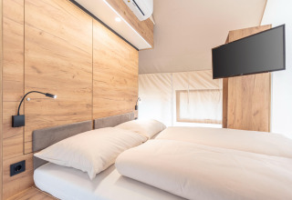 Camera moderna nella tenda safari di Chalets & Glamping Nassfeld 6, Austria, con letto matrimoniale e TV.