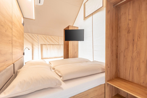 Interno di una tenda safari di lusso con letto matrimoniale, arredi in legno e TV a Nassfeld, Austria.