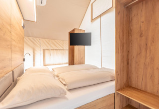 Interno di una tenda safari di lusso con letto matrimoniale, arredi in legno e TV a Nassfeld, Austria.