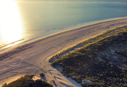Luchtfoto van een zonnig strand bij Ouddorp, Zuid-Holland, met duinen en schitterend kalm water.