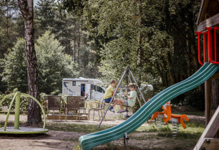 Bambini che giocano in un parco giochi accanto allo chalet Goudhaantje in Belgio, con camper sullo sfondo.