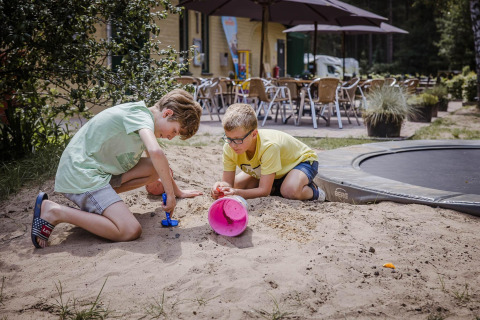 Twee jongens spelen in het zand bij een trampoline buiten chalet Vlaamse gaai in België.