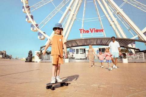En familie nyder tiden foran et pariserhjul ved 'The View', hvor et barn står på skateboard på pladsen.
