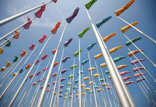 Maniche a vento colorate su alti pali ondeggiano nel vento in un alloggio glamping sotto il cielo azzurro.