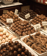 Variedad de trufas y bombones de chocolate expuestos en bandejas sobre un mostrador de mármol.