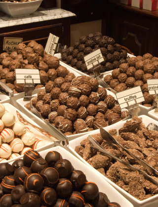 Assorted chocolate truffles and candies displayed in bowls on a marble counter at a chocolate shop.