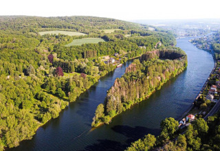 Luftfoto af en glamping-placering ved en flod omgivet af skov og hytter på begge bredder.