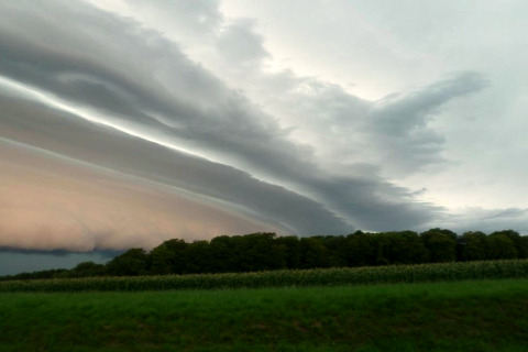 Dramatische wolkenformaties boven groene velden en bomen bij een glampingverblijf.