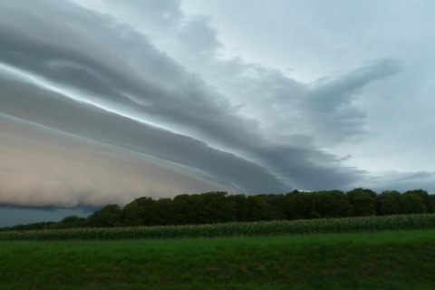 Dramatische Wolkenformationen über grünen Feldern und Bäumen bei einer Glamping-Unterkunft.