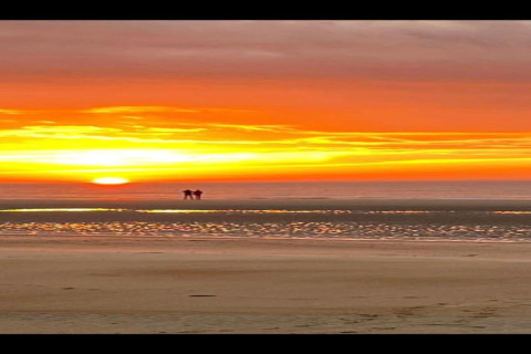 Twee personen beleven een prachtige zonsondergang aan het strand bij een glamping, lucht is oranjerood gekleurd.