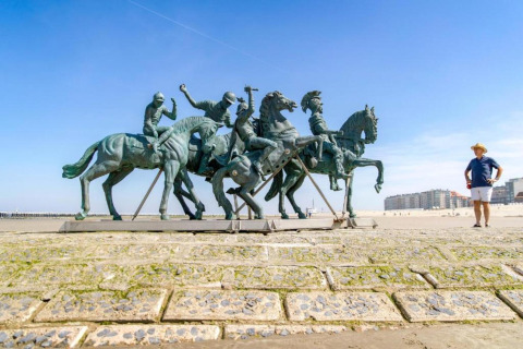 Un uomo accanto a una grande statua equestre sulla spiaggia vicino a un campeggio glamping, cielo sereno.