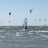 Windsurfisti e kitesurfisti in mare vicino a un glamping di un villaggio vacanze sotto cielo sereno.