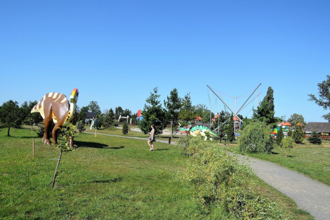 Un parque al aire libre con figuras de dinosaurios, senderos, césped verde y cielo azul despejado.