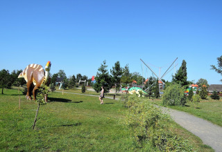 An outdoor park with large dinosaur statues, garden paths, green grass, and a clear blue sunny sky.