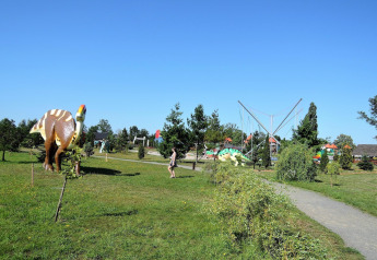Un parque al aire libre con figuras de dinosaurios, senderos, césped verde y cielo azul despejado.