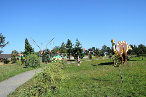 A person walks through a park with dinosaur models and trees under a clear blue sky at At «słonecznikiem» in Germany.