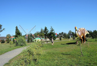 A person walks through a park with dinosaur models and trees under a clear blue sky at At «słonecznikiem» in Germany.