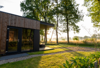 Udendørs billede af Boslodge 2 ved Hofparken Wiltershaar i Holland, omgivet af grønne træer og sollys.