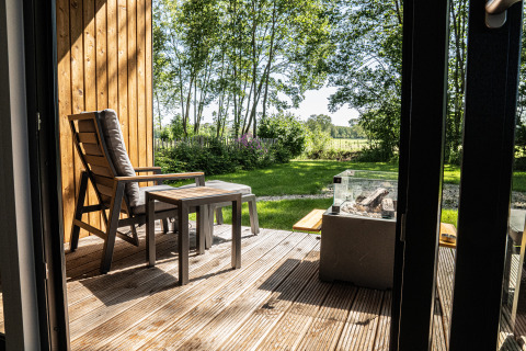 Deck with wooden chairs and views of green garden at Holiday villa Boslodge 2, Hofparken Wiltershaar, Netherlands.