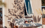 Cozy glamping accommodation patio with cushioned sofa, open window, and decorative pampas grass.