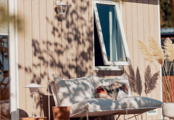 Gemütlicher Außenbereich eines Glamping-Zimmers mit Sofa, Kissen, Pflanzen und offenem Fenster.