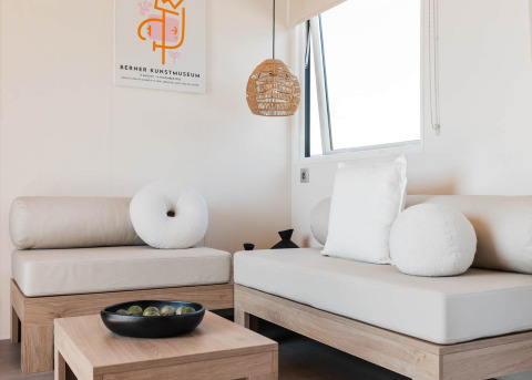 Moderne glamping accommodatie met lichte houten meubels, witte kussens en minimalistische inrichting.