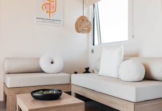 Moderne glamping accommodatie met lichte houten meubels, witte kussens en minimalistische inrichting.