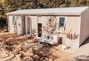 Außenaufnahme einer Glamping-Unterkunft mit Holzterrasse, Sitzbank und Pflanzen, umgeben von Bäumen.