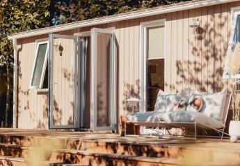 Solrigt glampingophold med moderne terrasse, dobbeltseng og åbne døre til naturoplevelser.