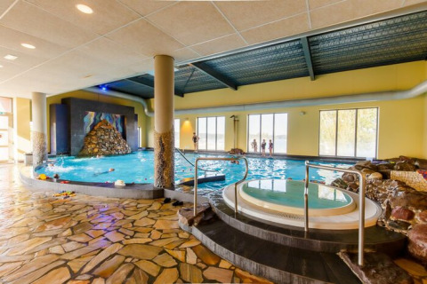 Espace piscine intérieure dans un hébergement glamping avec jacuzzi, sol en pierre et grandes fenêtres.