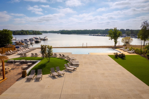 Vue d'un site de glamping de luxe avec transats, piscine et bateaux amarrés sur un lac paisible.