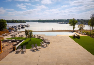 Uitzicht op een luxueuze glampingplaats met ligstoelen, zwembad en boten aan een vredig meer.