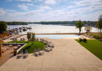 Vista de un lujoso sitio de glamping con tumbonas, piscina y barcos atracados en un lago tranquilo.