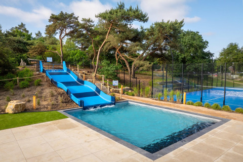 Außenpool mit blauer Wasserrutsche und Tennisplatz bei Sunset Lodge im Vakantiepark Leukermeer, Niederlande.