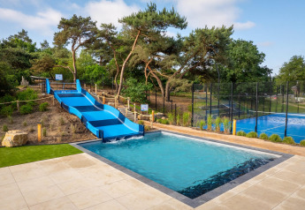 Piscina exterior con tobogán azul y cancha de tenis en Sunset Lodge, Vakantiepark Leukermeer, Países Bajos.