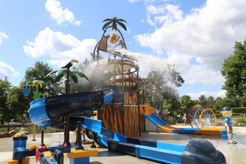 Aire de jeux aquatique avec toboggans et fontaines dans un site de glamping par une journée ensoleillée.