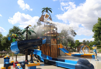 Parque acuático infantil con toboganes, fuentes y figuras en un alojamiento glamping en día soleado.