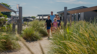 A family walks through the dunes at Dune Lodge in EuroParcs Parc du Soleil, Netherlands, on a sunny summer day.