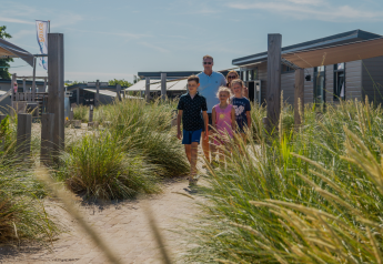 Una familia camina entre dunas en el Dune Lodge de EuroParcs Parc du Soleil en los Países Bajos en un día soleado.