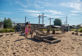 Kinderen spelen op een zandige speelplaats bij Dune Lodge, EuroParcs Parc du Soleil, Nederland, zonnige dag.